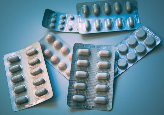 Photographie de différentes plaquettes de médicaments de différentes formes et tailles, dans les tons de bleus et de gris froids.